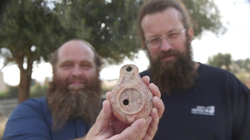 החוקרים מיכאל טשרנין ובנימין סטורצ'ן מחזיקים את הנר הנדיר (צילום: אמיל אלג'ם, רשות העתיקות)